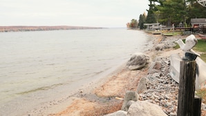A lakeside view with a wooden dock, rocks, and a distant shoreline with trees. - The Cottage at Hubbard Lake (Hubbard Lake)