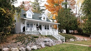 A two-story house with a front porch, a small attached garage, and a stone retaining wall. - The Cottage at Hubbard Lake (Hubbard Lake)