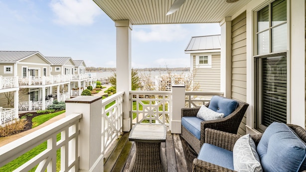 A covered porch with wicker furniture and a view of a residential area. - Waterfront Condo, Pool, Walk to Downtown (Saugatuck)