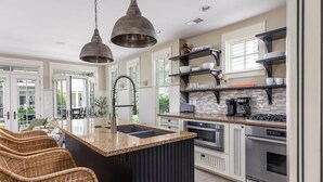 A modern kitchen with a central island, stainless steel appliances, and a breakfast bar with wicker chairs. - Waterfront Condo, Pool, Walk to Downtown (Saugatuck)