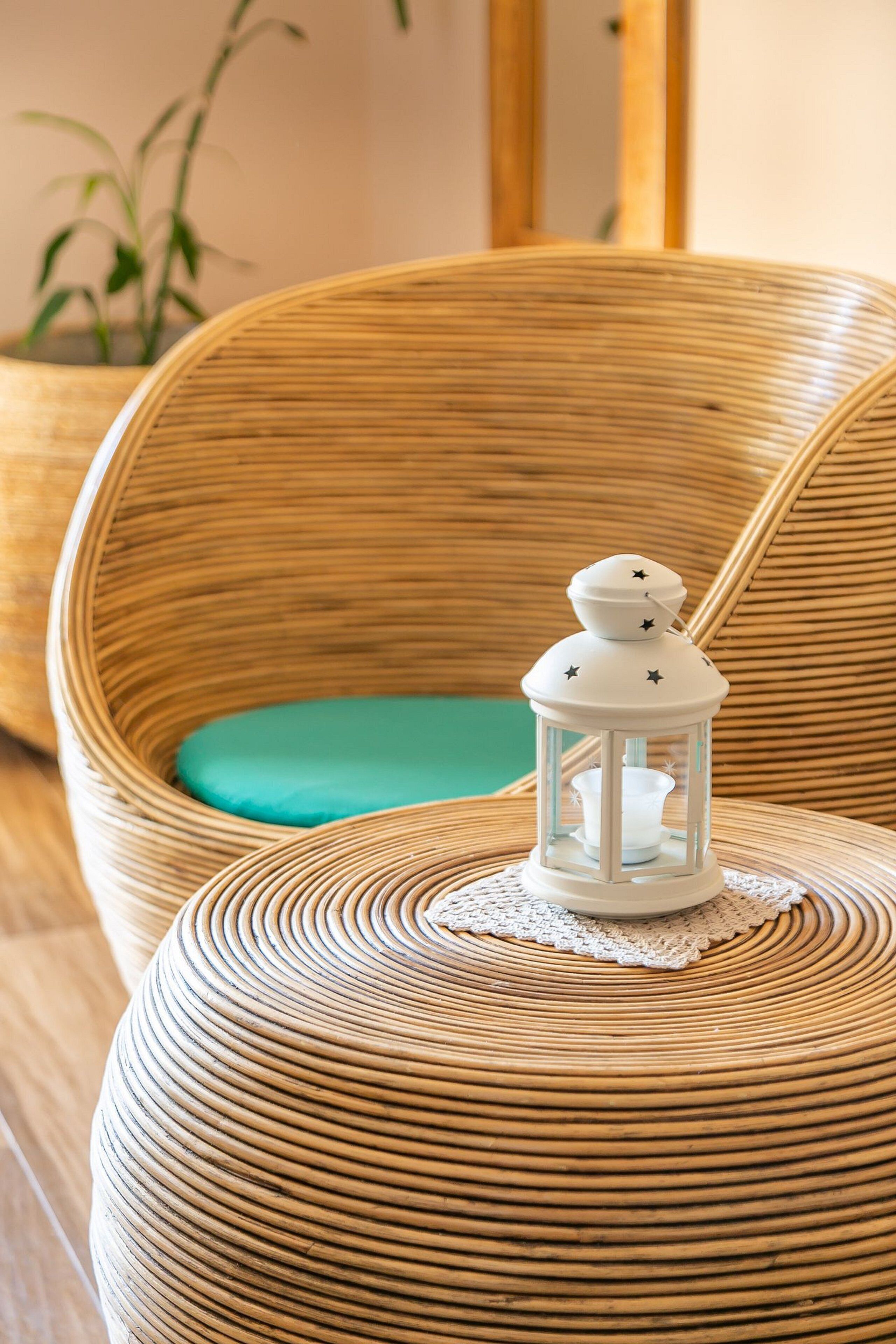 A wicker chair with a teal cushion, a small white lantern with stars, and a doily on a round table.