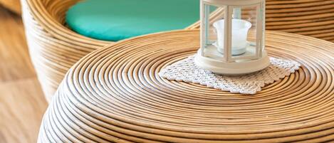A wicker chair with a teal cushion, a small white lantern with stars, and a doily on a round table.