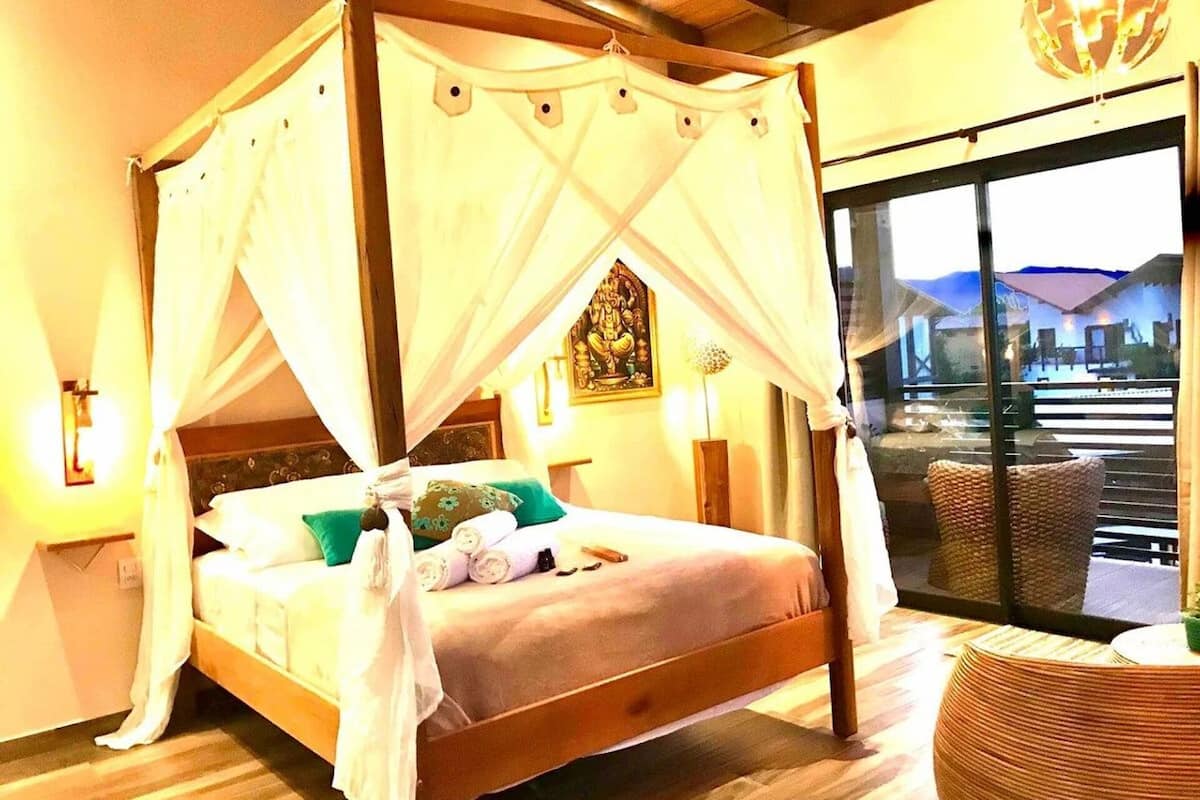 A four-poster bed with a canopy, a wooden headboard, and a view of the outside through a glass door.