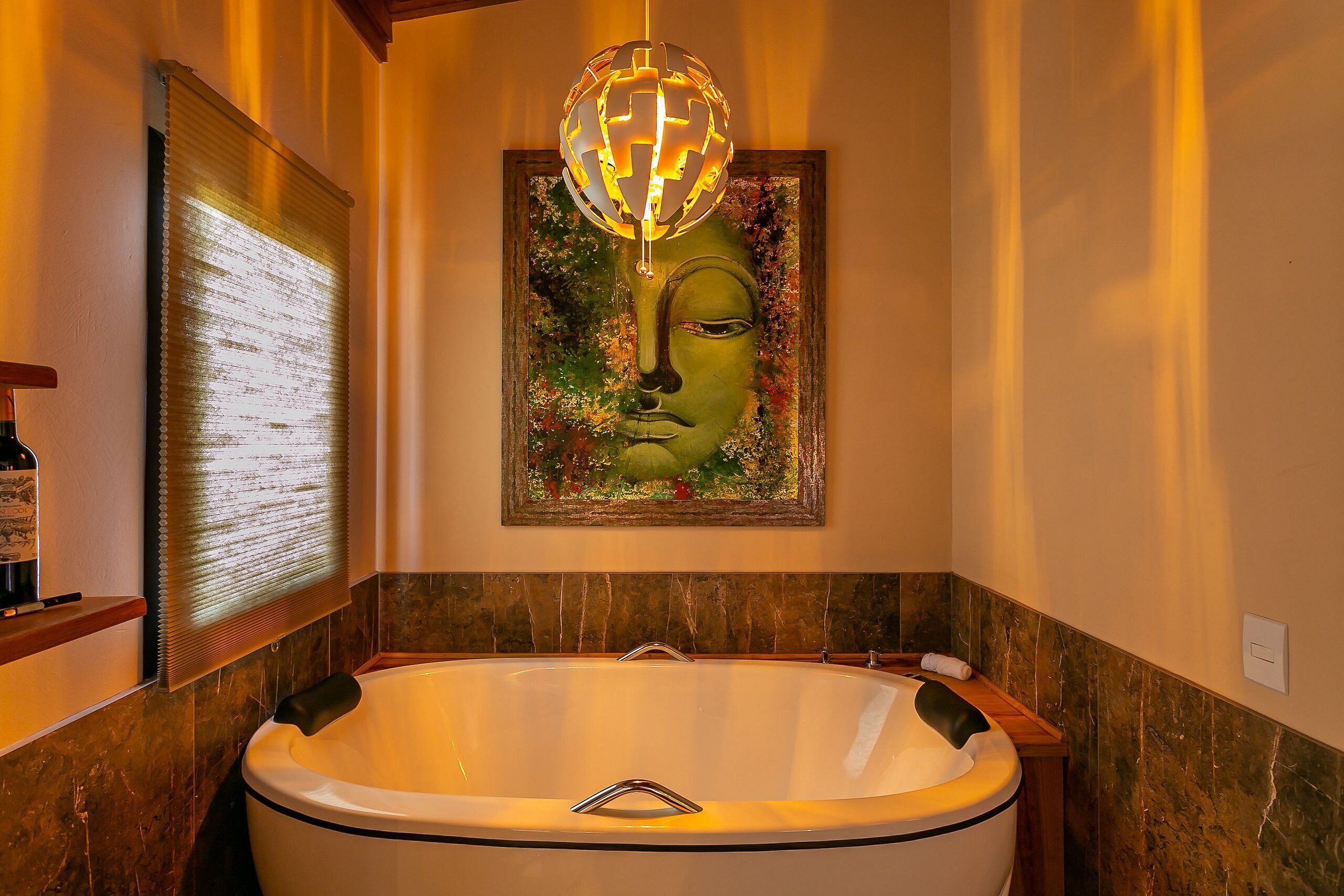 Un baño con una bañera grande, una obra de arte enmarcada encima y una ventana con persianas.