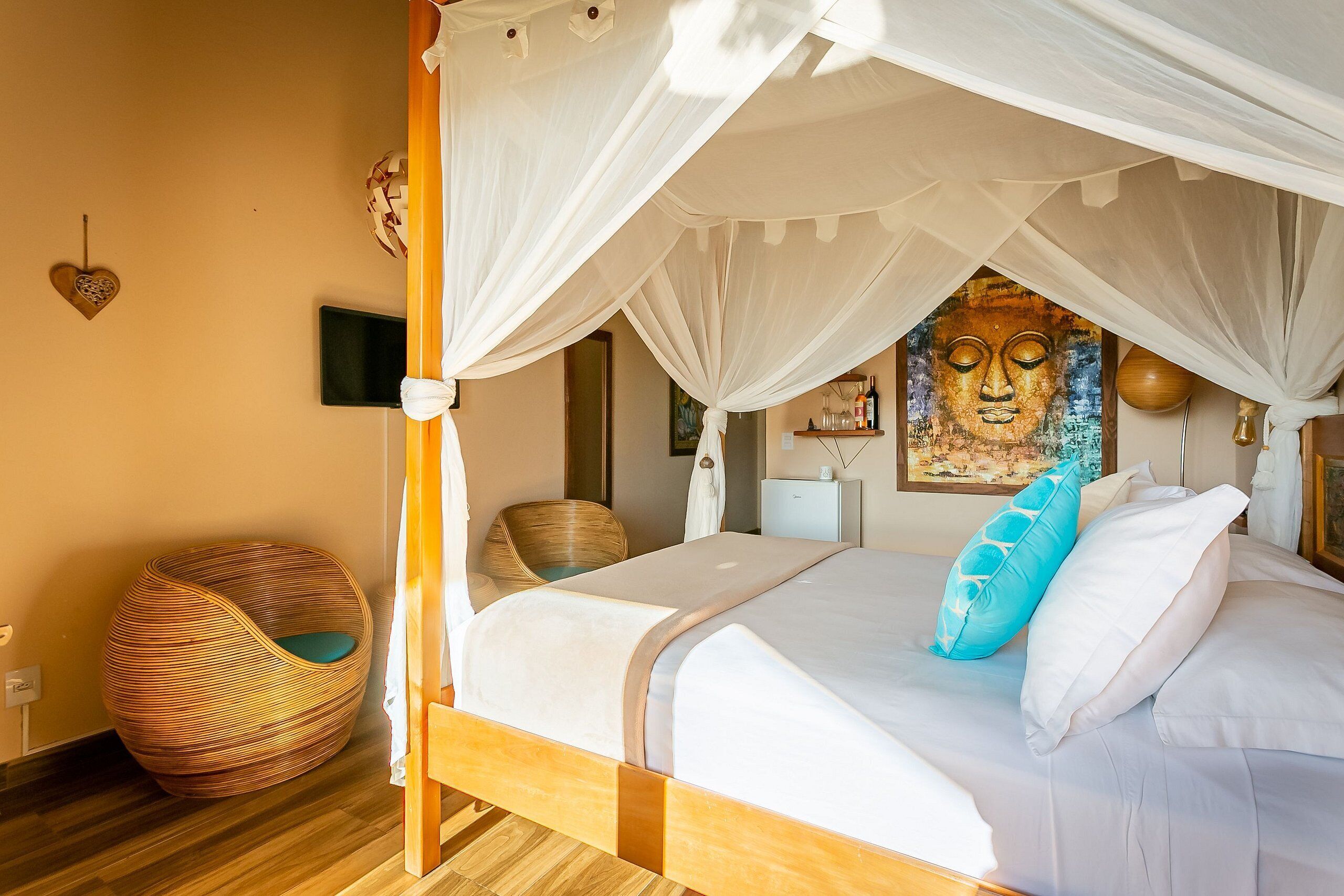 A four-poster canopy bed with a large painting above it, a wicker chair, and a heart-shaped decoration on the wall.