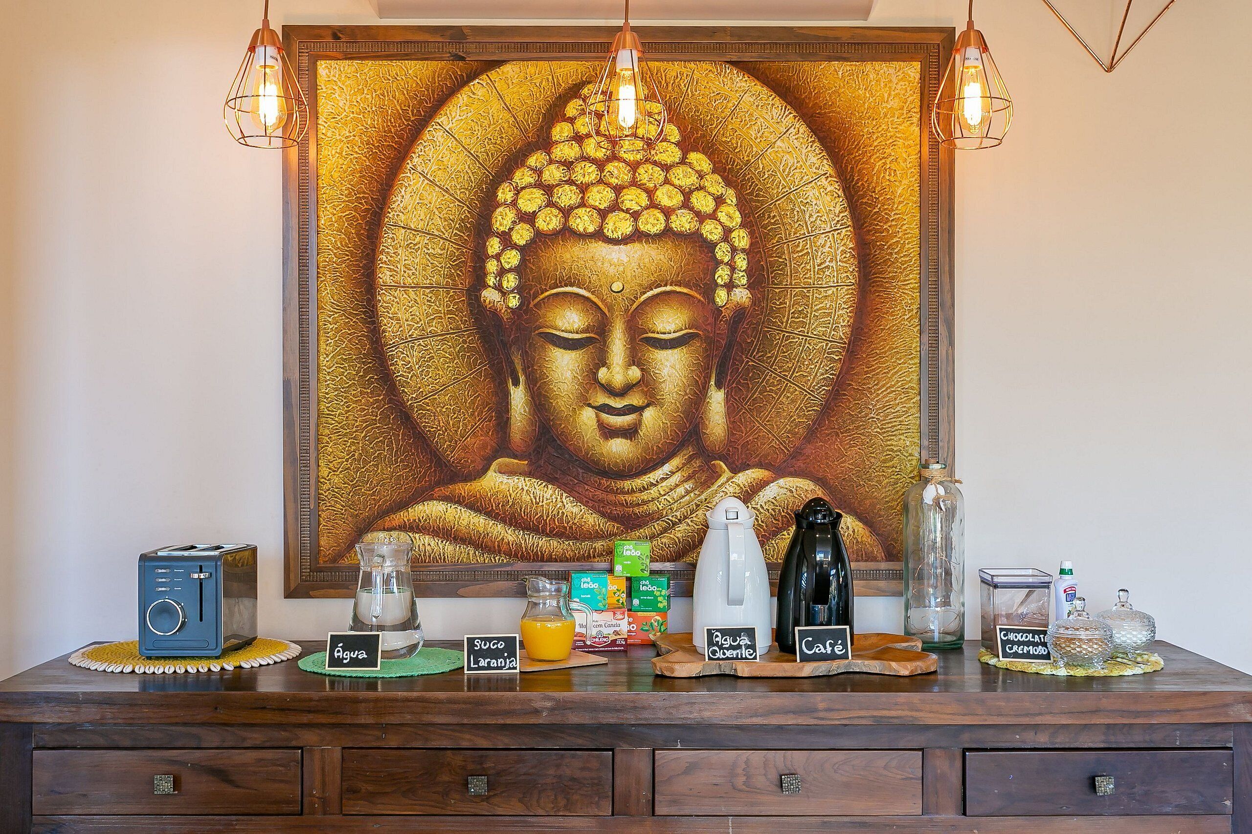 A Buddha statue with a golden halo, surrounded by various coffee and tea-making equipment on a wooden counter.