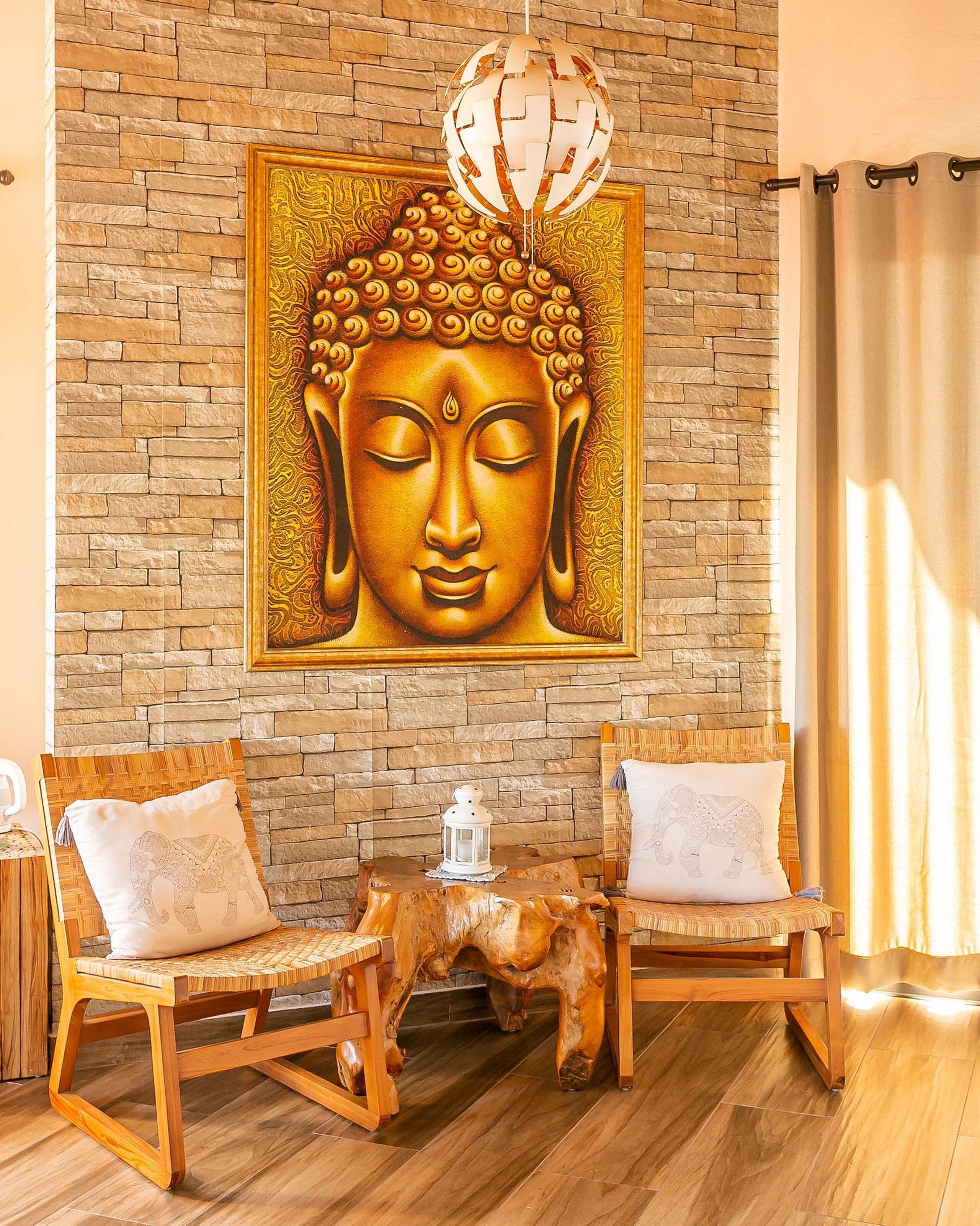 A room with a Buddha mural, two wooden chairs with cushions, a small wooden table, and a stone wall.