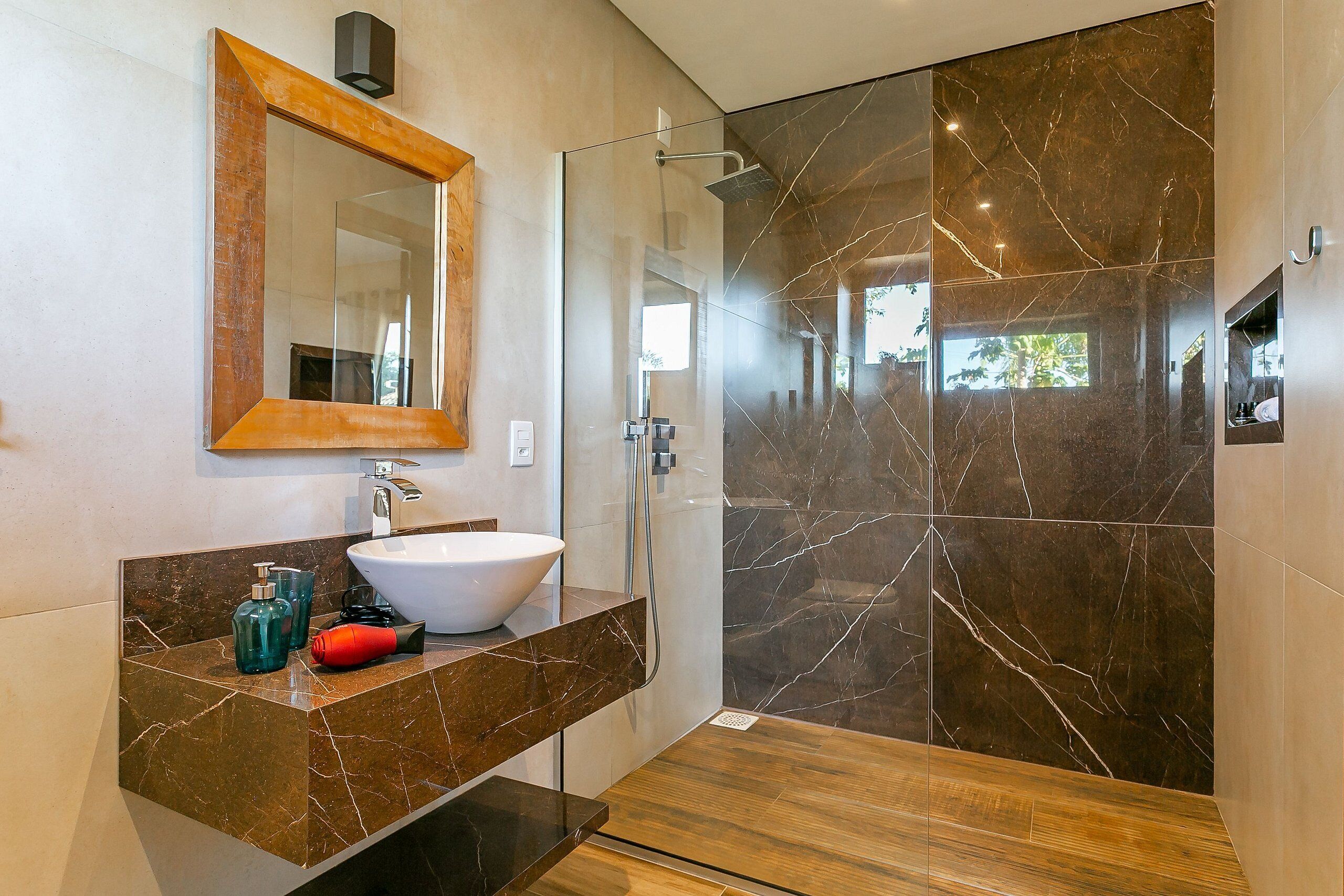 A modern bathroom with a glass shower enclosure, a marble-tiled wall, and a wooden floor.