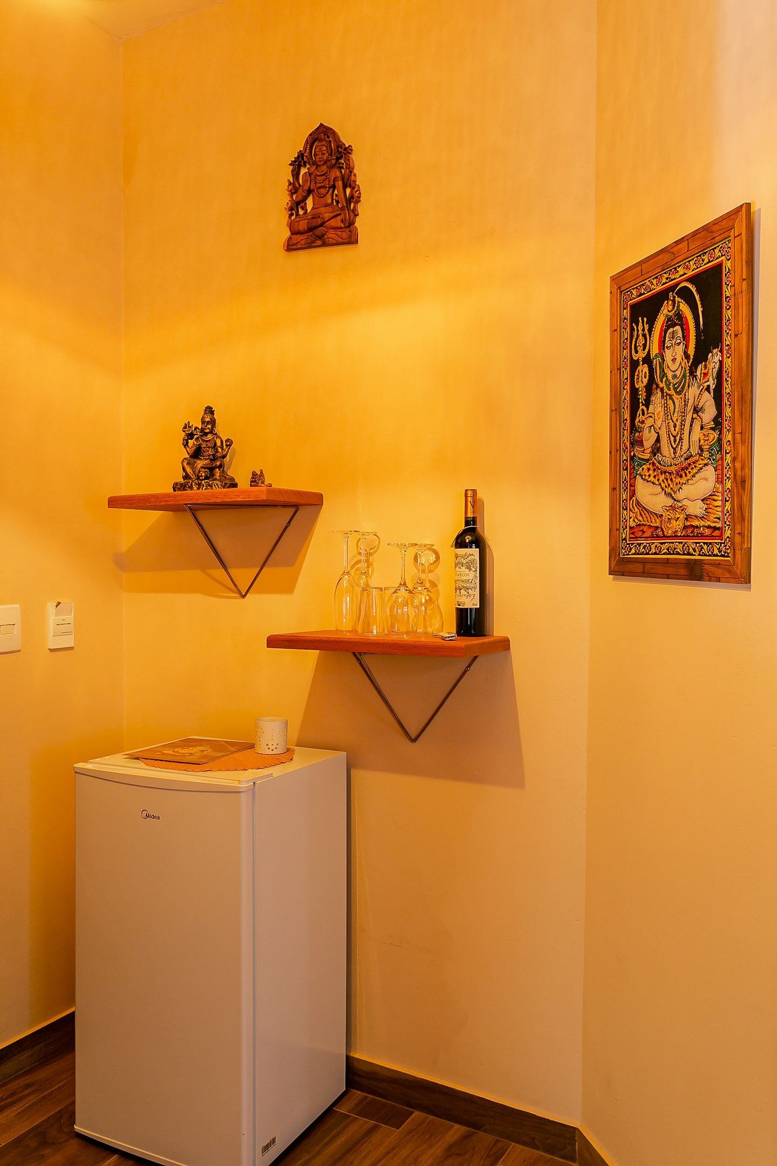 Eine kleine Küche mit Kühlschrank, Holzregalen und einem gerahmten Kunstwerk an der Wand.