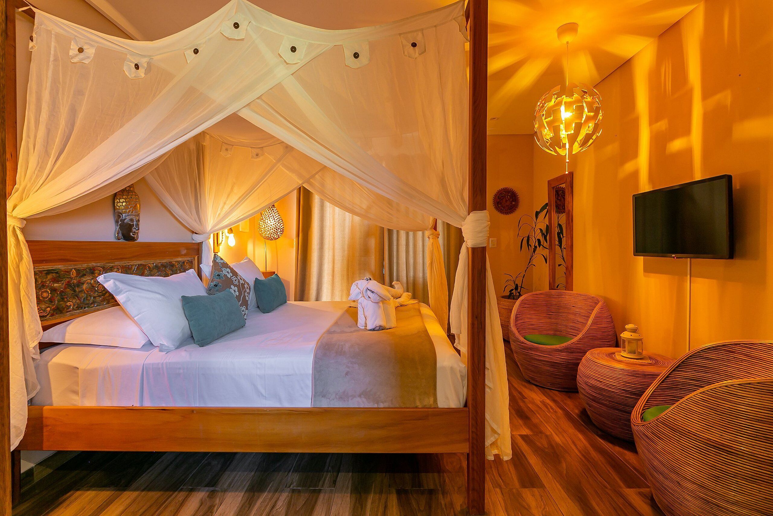 A four-poster canopy bed with white linens and decorative pillows, a wooden headboard, and a bedside table with a lamp.