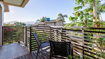 Una terraza de madera con sillas de mimbre, una planta en maceta y vistas a una cordillera.