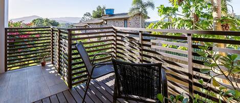 A wooden deck with wicker chairs, a potted plant, and a view of a mountain range.