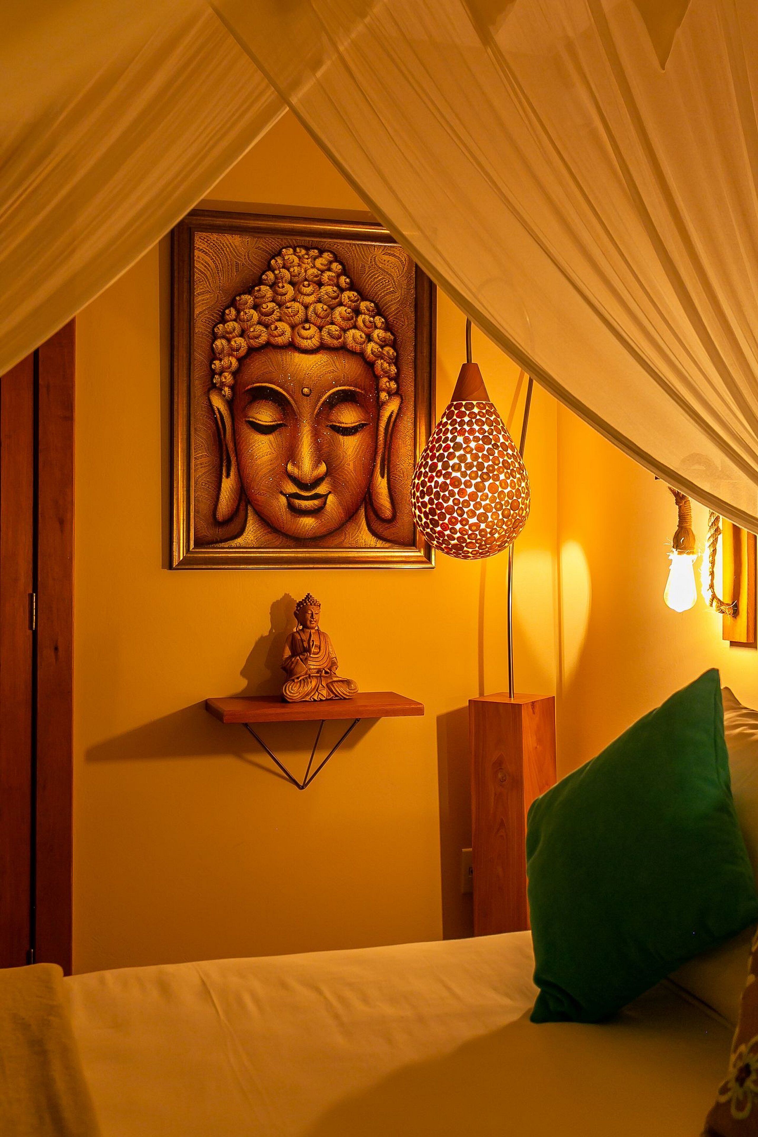 Una habitación con una estatua de Buda en un estante, una lámpara colgante y un cojín verde sobre la cama.