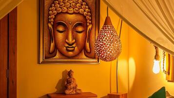 Una habitación con una estatua de Buda en un estante, una lámpara colgante y un cojín verde sobre la cama.