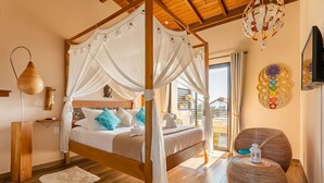 A four-poster canopy bed with a white bedspread and blue pillows, a round wooden side table with a lantern, and a decorative wall piece. - Shiva Boutique Hotel - Praia do Rosa (Imbituba)