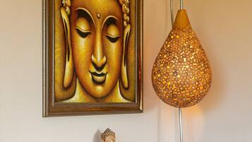 Una estatua de Buda, un cuadro enmarco con Buda y una lámpara decorativa sobre un estante de madera frente a una pared lisa.