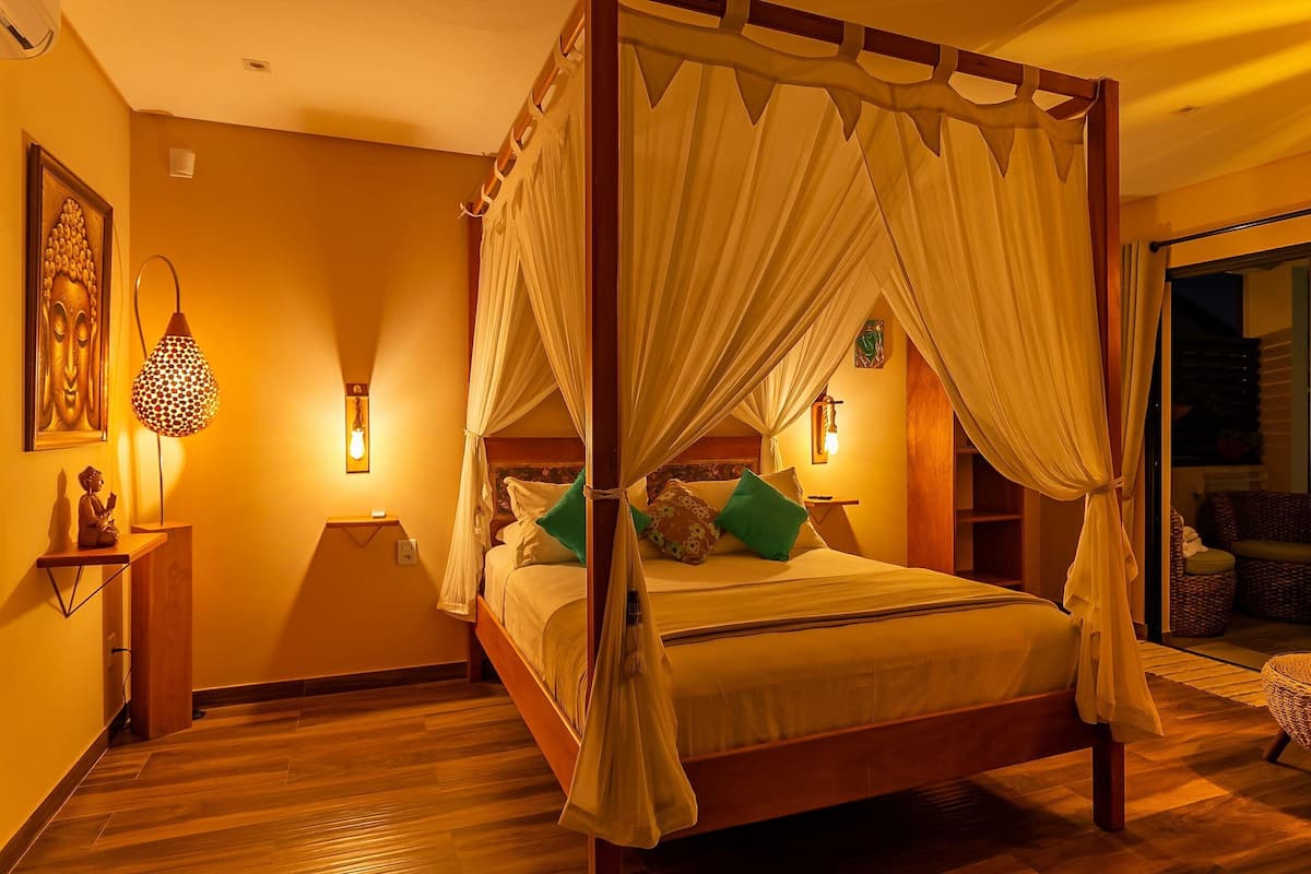 A four-poster canopy bed with a wooden frame, a bedside table with a lamp, and a wall-mounted light fixture.