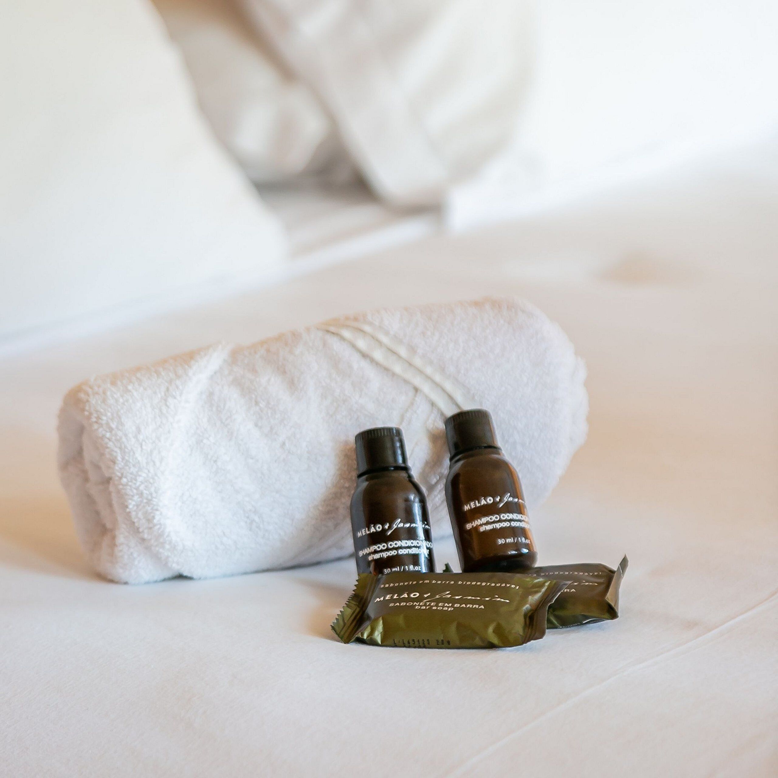 A neatly made bed with a white towel and two bottles of shampoo and soap.