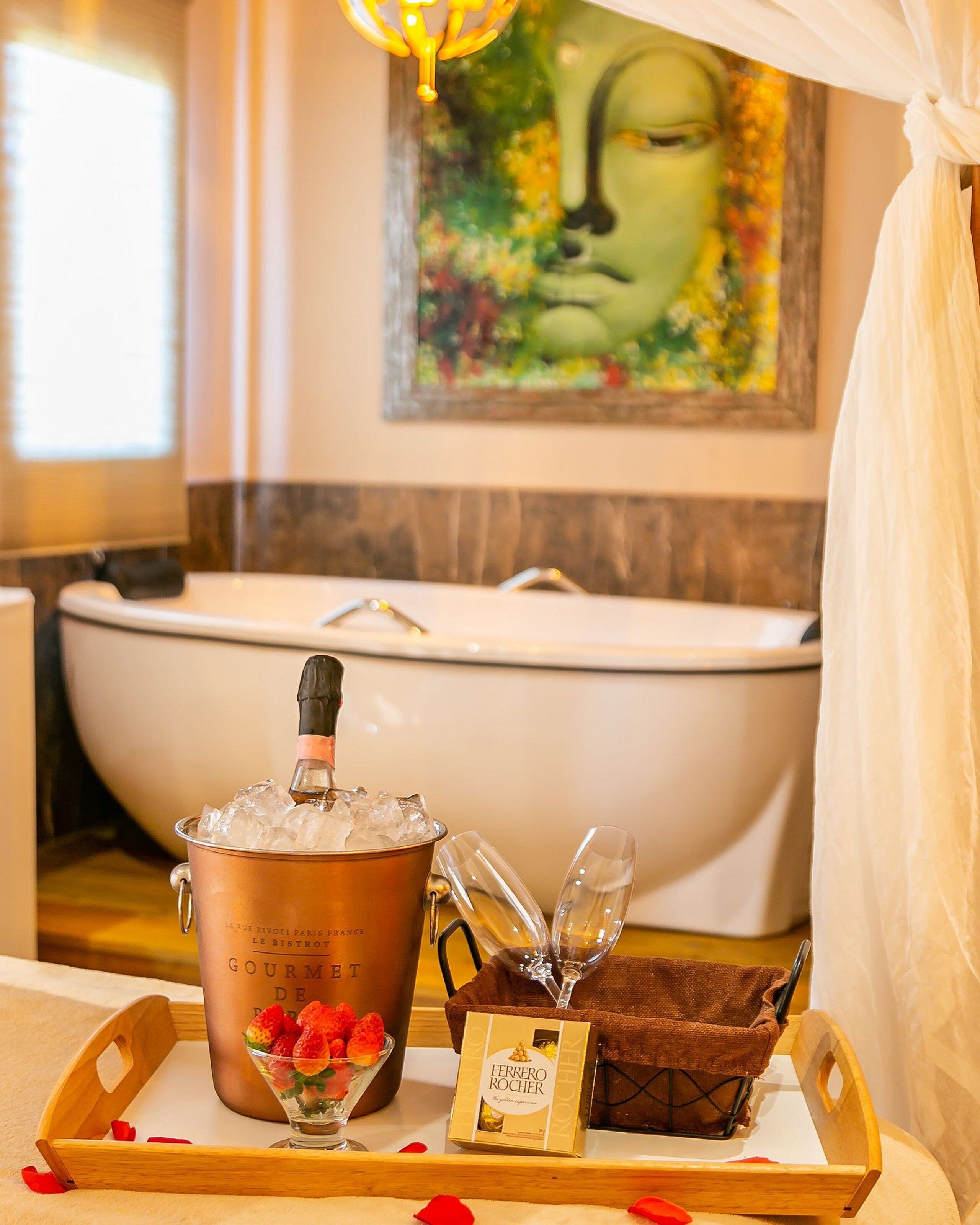 Un baño con bañera, una olla de cobre, copas de champán, una bandeja con fresas y una caja de Ferrero Rocher.