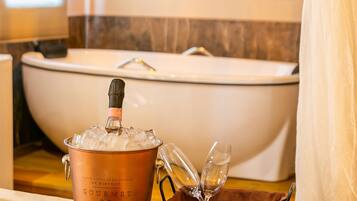 Un baño con bañera, una olla de cobre, copas de champán, una bandeja con fresas y una caja de Ferrero Rocher.