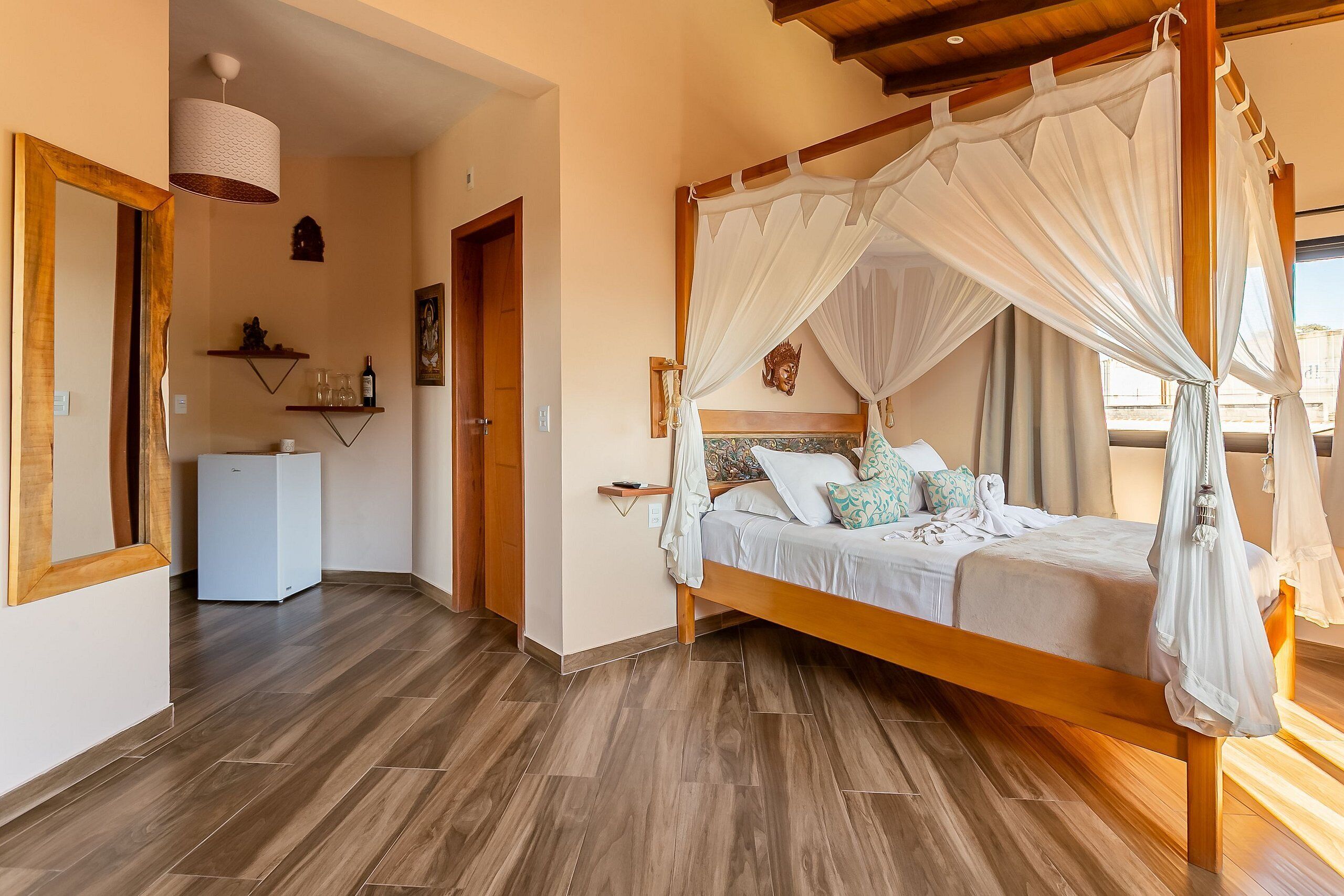 A bedroom with a wooden four-poster bed, a bedside table, a nightstand, a wall-mounted shelf with decorative items, and a door leading to another room.