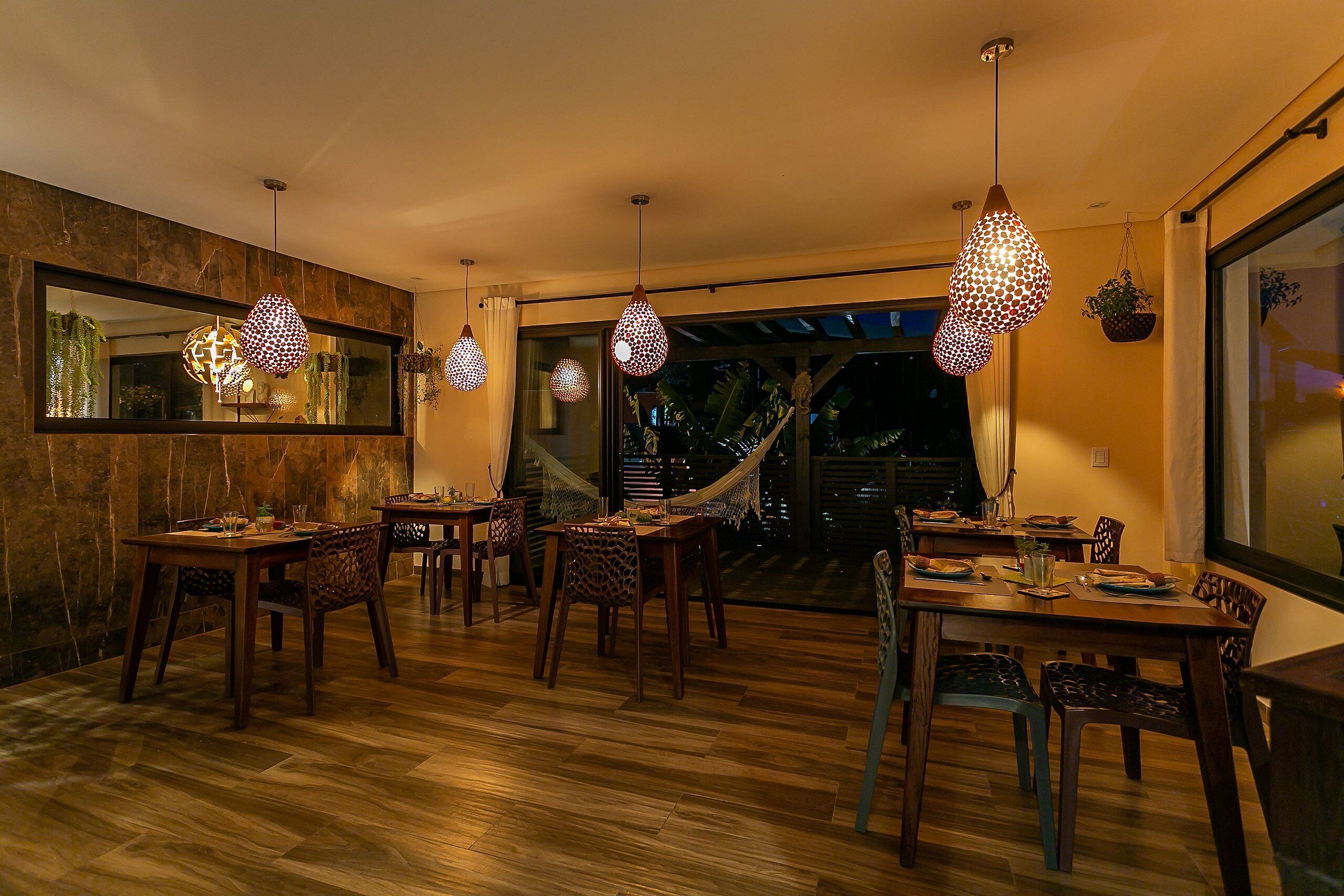 Un comedor con mesas y sillas de madera, lámparas colgantes y un espejo grande en la pared.