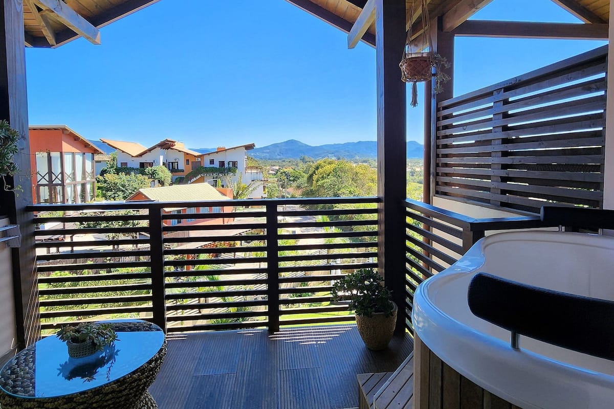 A covered outdoor area with a wooden deck, a hot tub, and a view of houses and mountains in the background.