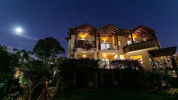 Un edificio de varios pisos con balcones, una hamaca y un cielo nocturno estrellado.