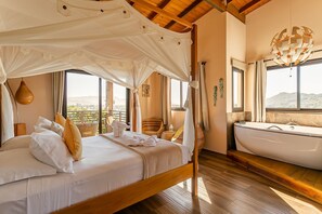 Ein Schlafzimmer mit Baldachinbett, einer Badewanne und großen Fenstern mit Blick auf die Hügel.