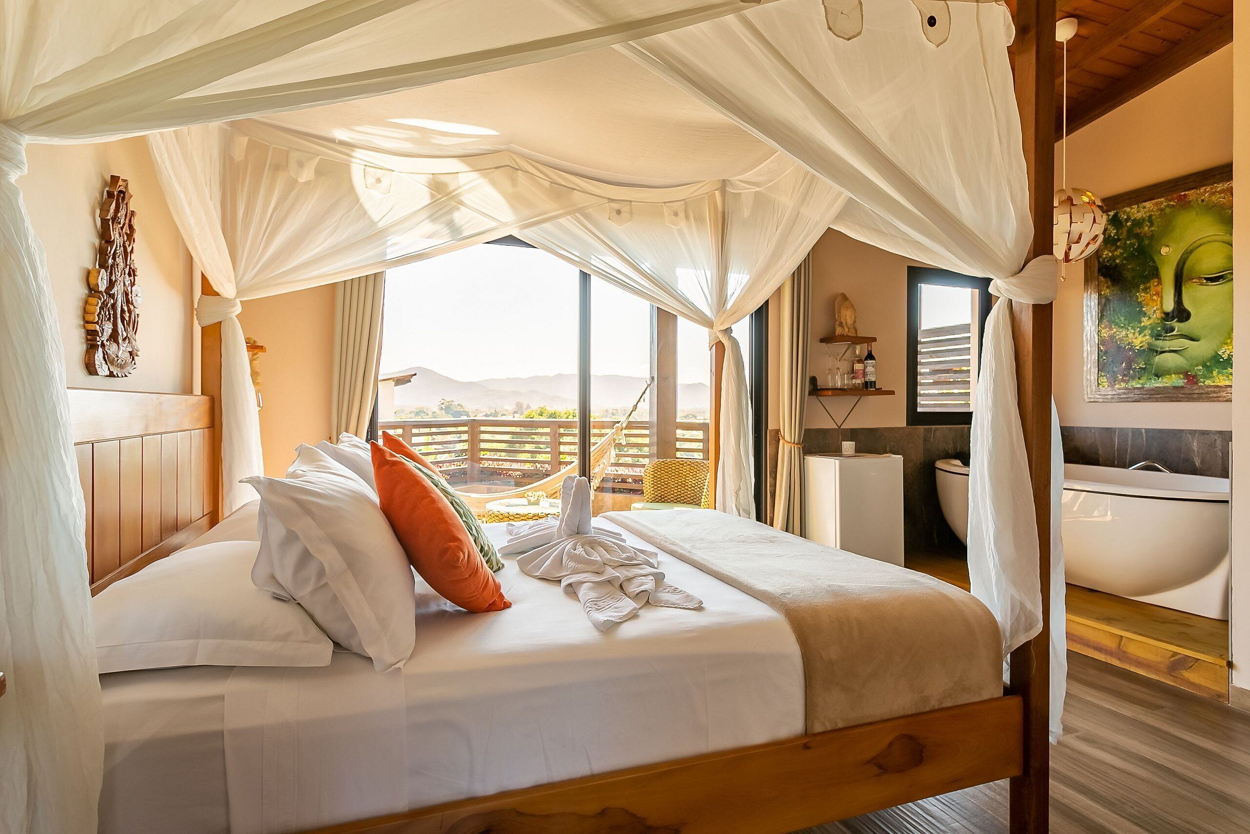 A bed with a canopy, a view of the mountains, a painting, and a bathroom with a bathtub.