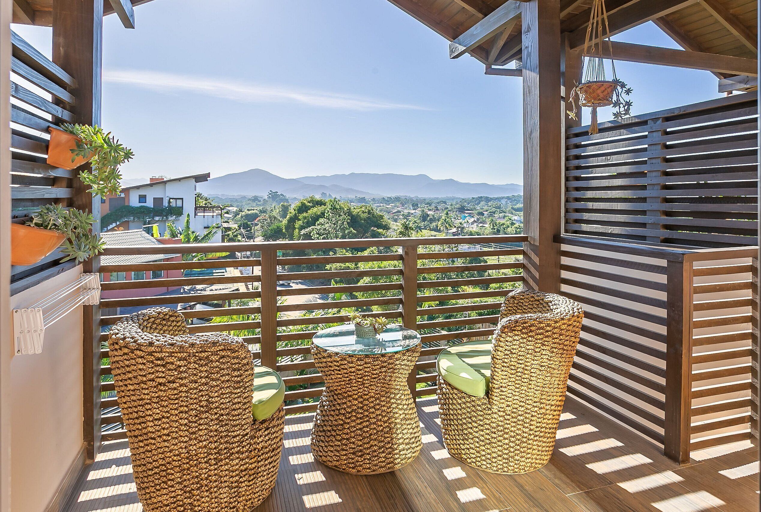 A balcony with wicker furniture, a view of a mountainous landscape, and a wooden railing.