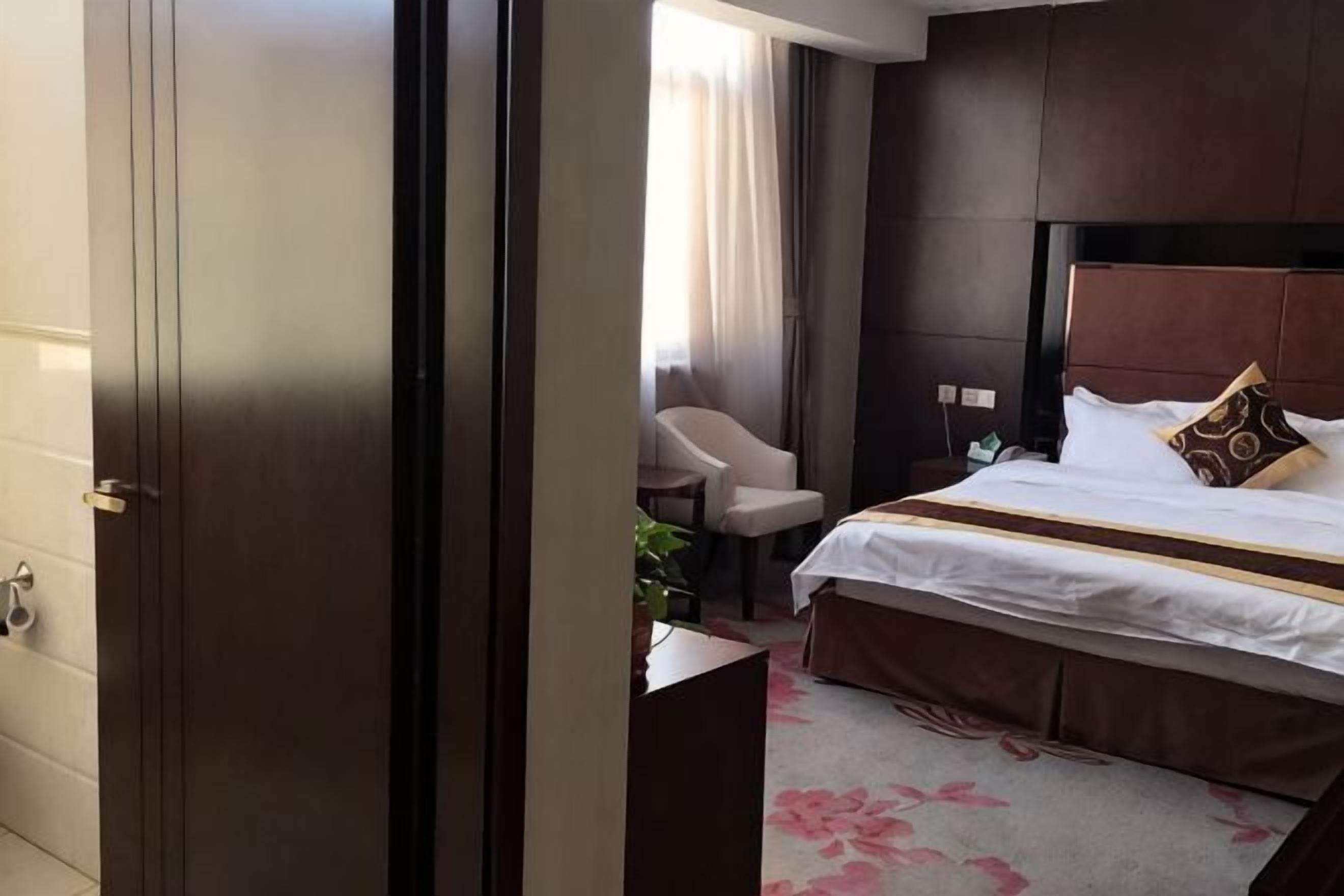 Una habitación de hotel con cama, una silla, un escritorio y una ventana con cortinas.