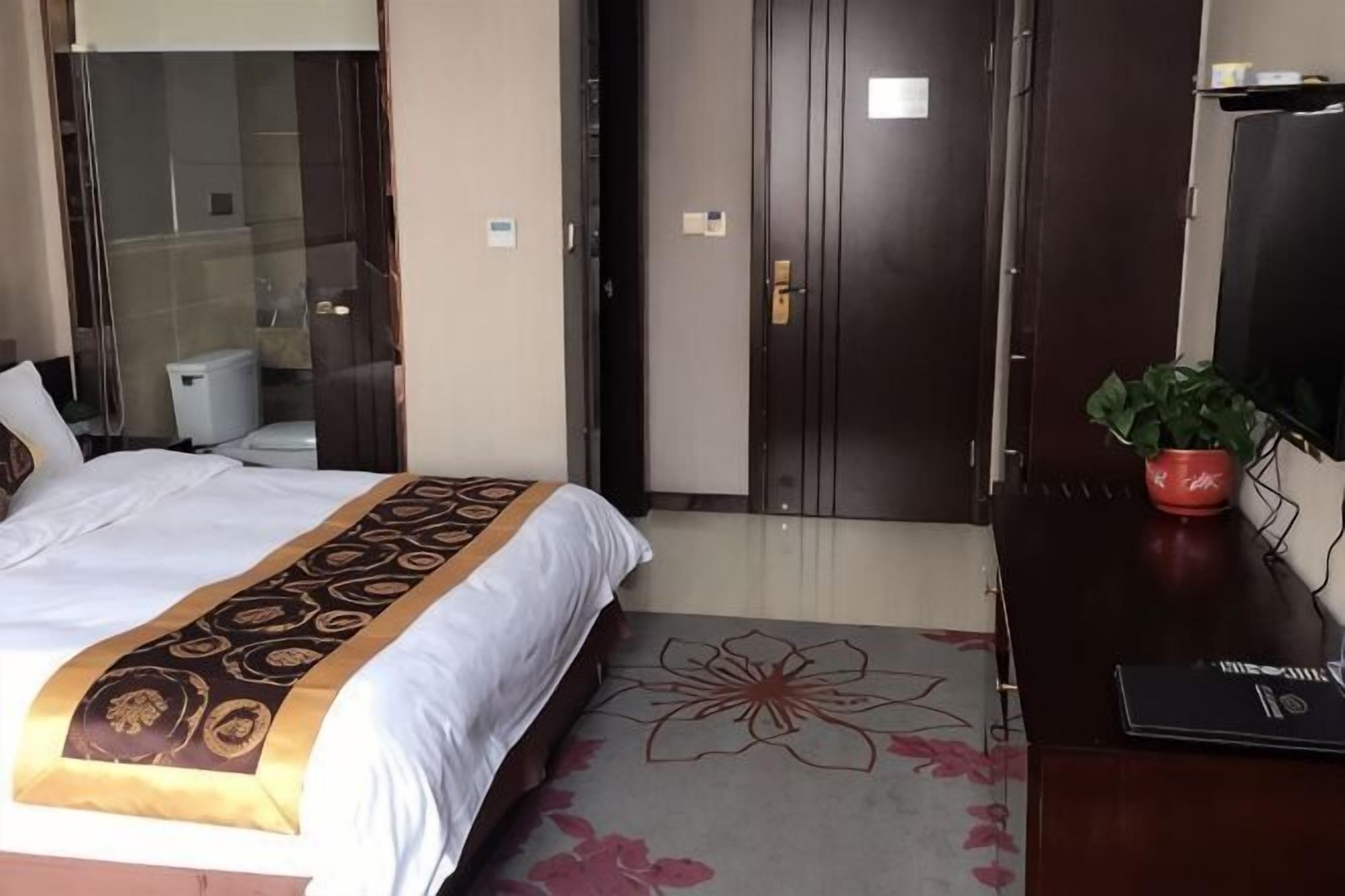 Quarto de hotel com cama, mesa com planta, televisão e porta.