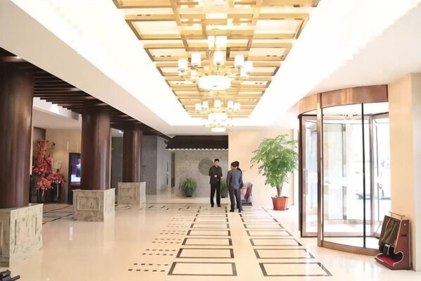 A hotel lobby with a modern design, featuring a wooden ceiling, a reception desk, and a large potted plant.