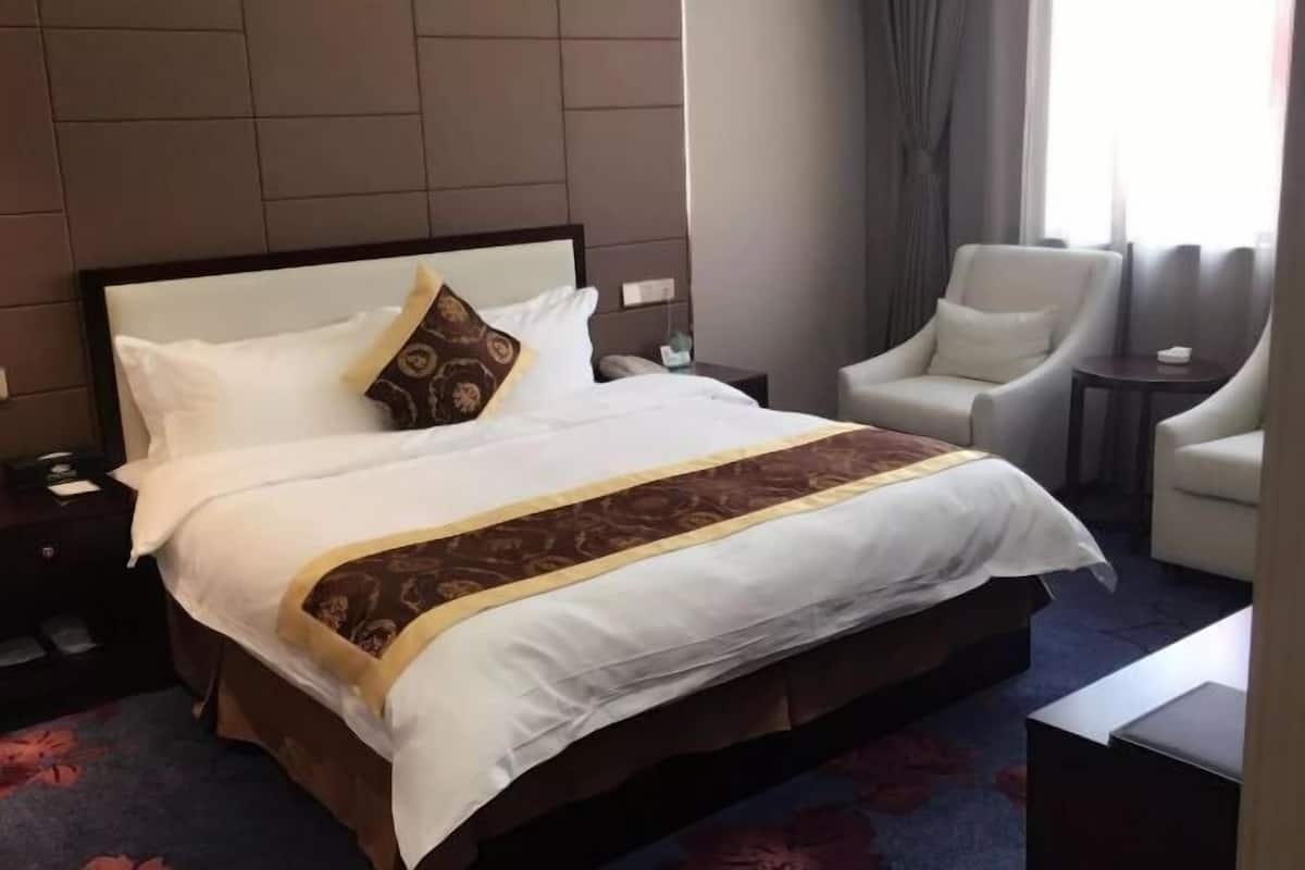 A hotel room with a large bed, a nightstand, a chair, and a small table.