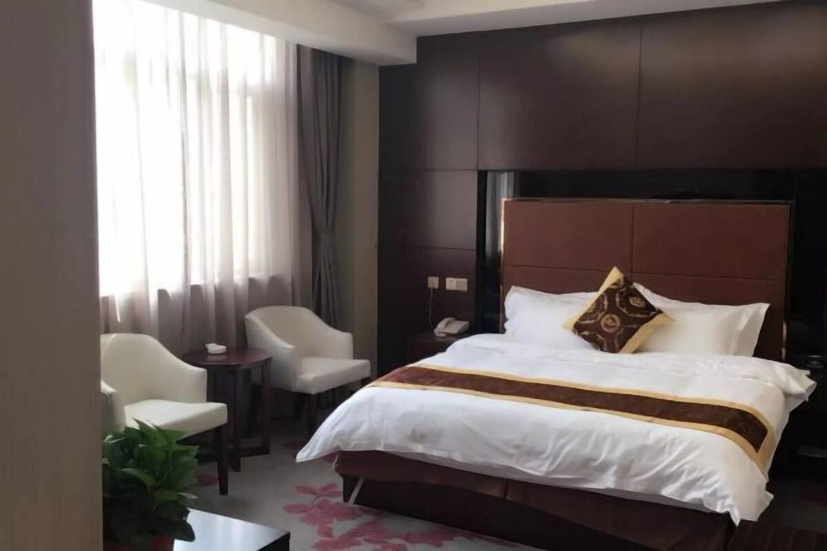 A hotel room with a large bed, a bedside table, a chair, and a window with curtains.