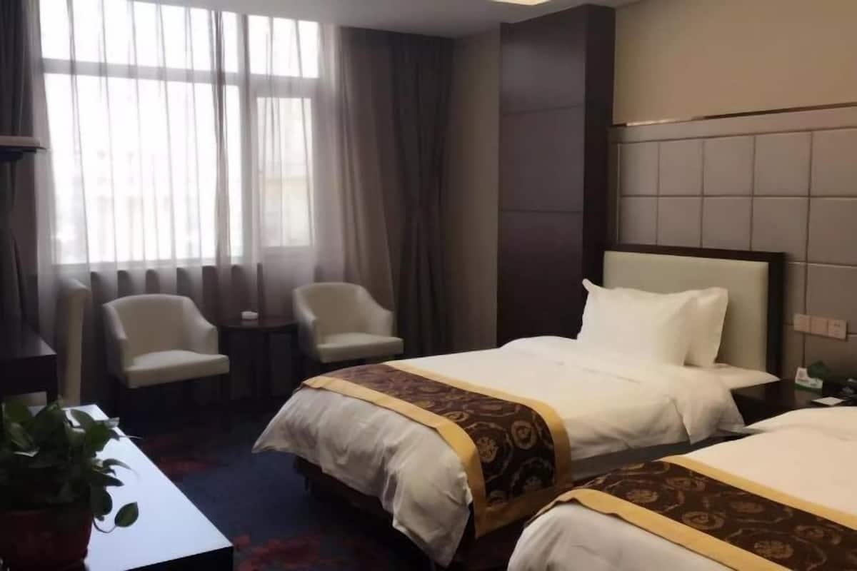 A hotel room with two beds, a small table, two chairs, and a potted plant.