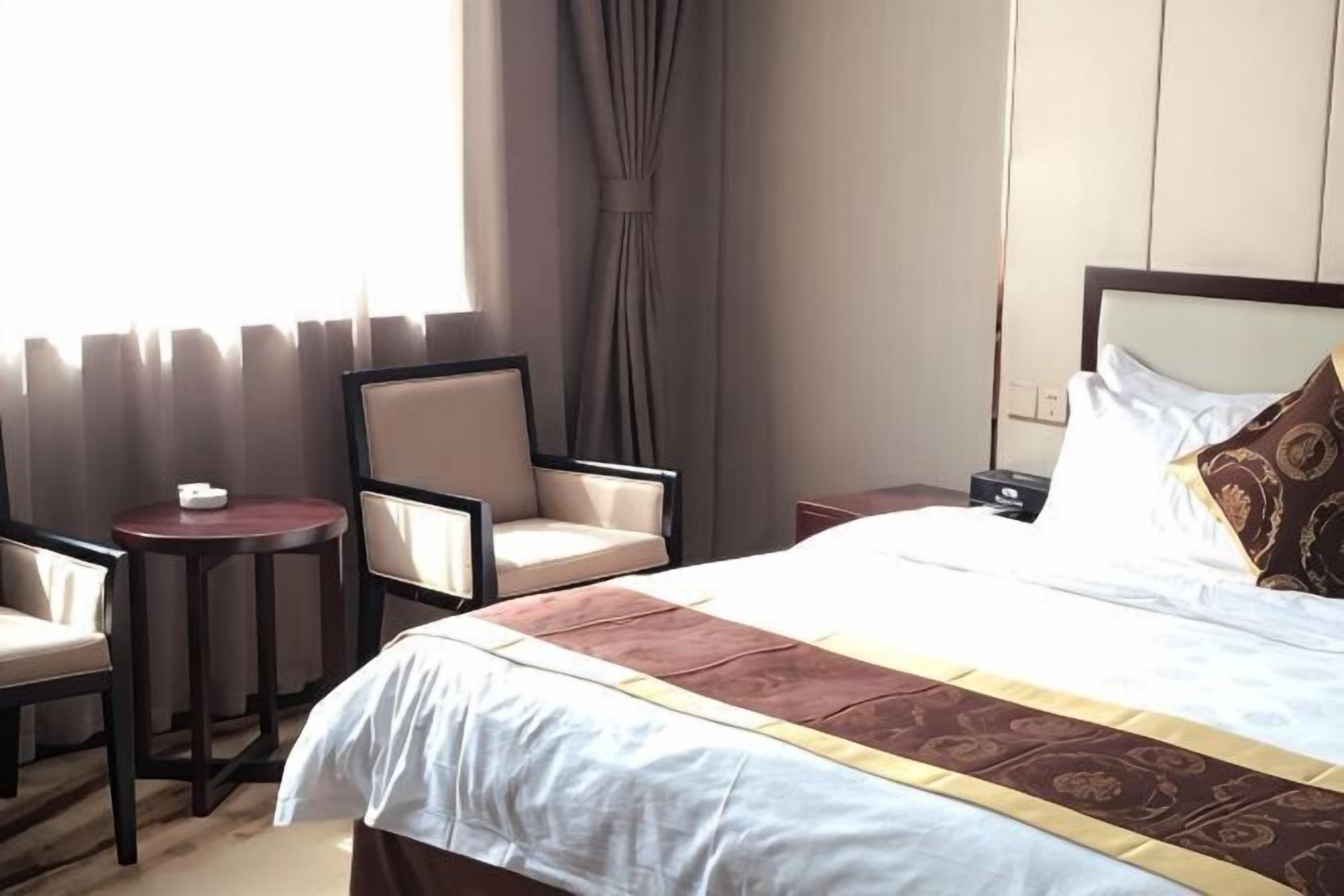 A hotel room with a bed, two chairs, a small table, a nightstand, and a window with curtains.