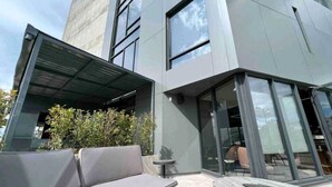 A modern building with a covered outdoor seating area, large windows, and a visible interior space.