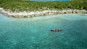 A clear turquoise sea with a rocky shoreline and dense green vegetation. - Luxumas: Unveiling the Extraordinary - All-New, Fully-Staffed Luxury Eco Resort (Exumas)