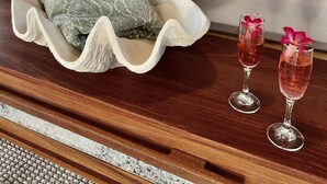 A neatly made bed with a gray blanket and pillows, a wooden tray with a folded towel, and two glasses of red drink with a flower garnish on a wooden table. - Luxumas: Unveiling the Extraordinary - All-New, Fully-Staffed Luxury Eco Resort (Exumas)