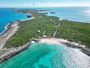 An aerial view of a tropical island with a clear turquoise sea, a sandy beach, and a dense green forest. There are several small buildings scattered across the island, likely accommodations. - Luxumas: Unveiling the Extraordinary - All-New, Fully-Staffed Luxury Eco Resort (Exumas)