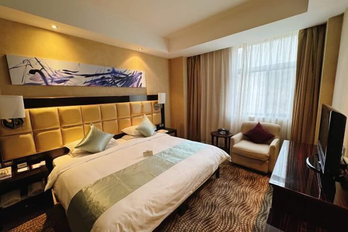 Una habitación de hotel con una cama grande, un escritorio, una silla, un televisor y un cuadro en la pared.