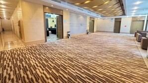 A spacious hotel lobby with a patterned carpet, a reception area, and a modern ceiling design.