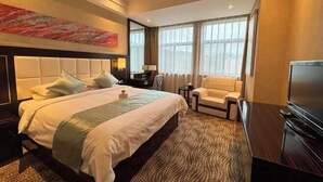 A hotel room with a large bed, a television, a sofa, and a window with curtains.