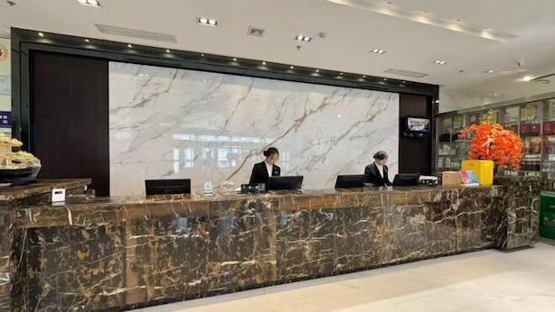 A marble reception desk with two staff members, a digital screen, and a large floral arrangement.