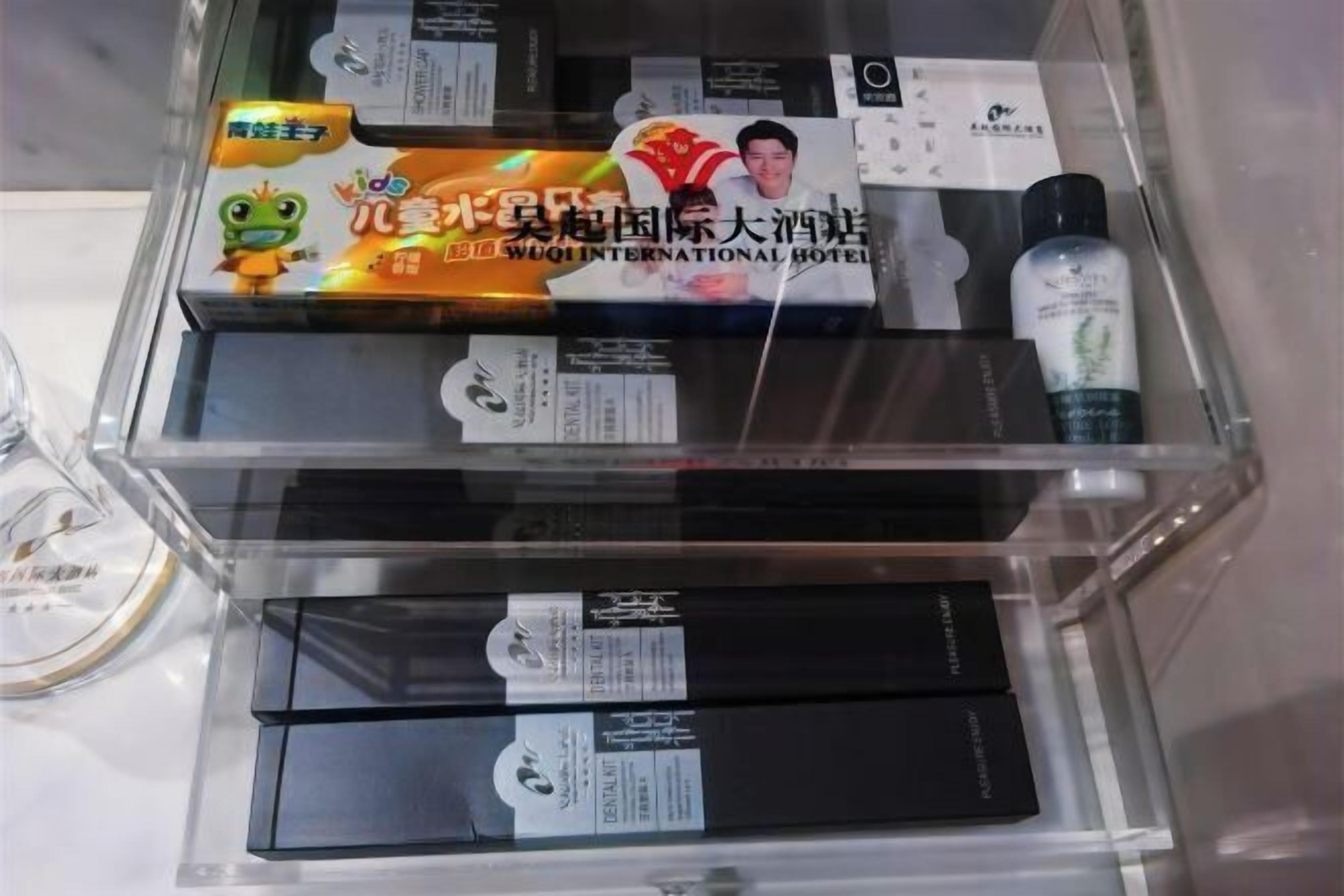 A hotel room with a minibar containing various items including a bottle of water, a box of snacks, and a bottle of lotion.