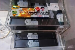 A hotel room with a minibar containing various items including a bottle of water, a box of snacks, and a bottle of lotion. - Wuqi International Hotel (Wuqi)