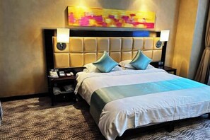 A hotel room with a large bed, two bedside tables, a headboard with a light panel, and a colorful abstract painting above the bed. - Wuqi International Hotel (Wuqi)