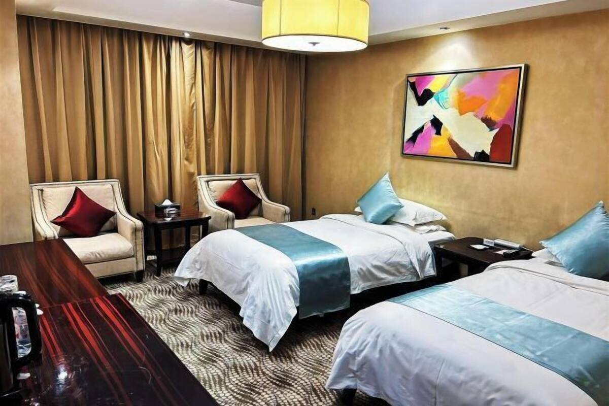 Habitación de hotel con dos camas, un escritorio de madera, una silla, una mesita pequeña y un cuadro abstracto colorido en la pared.
